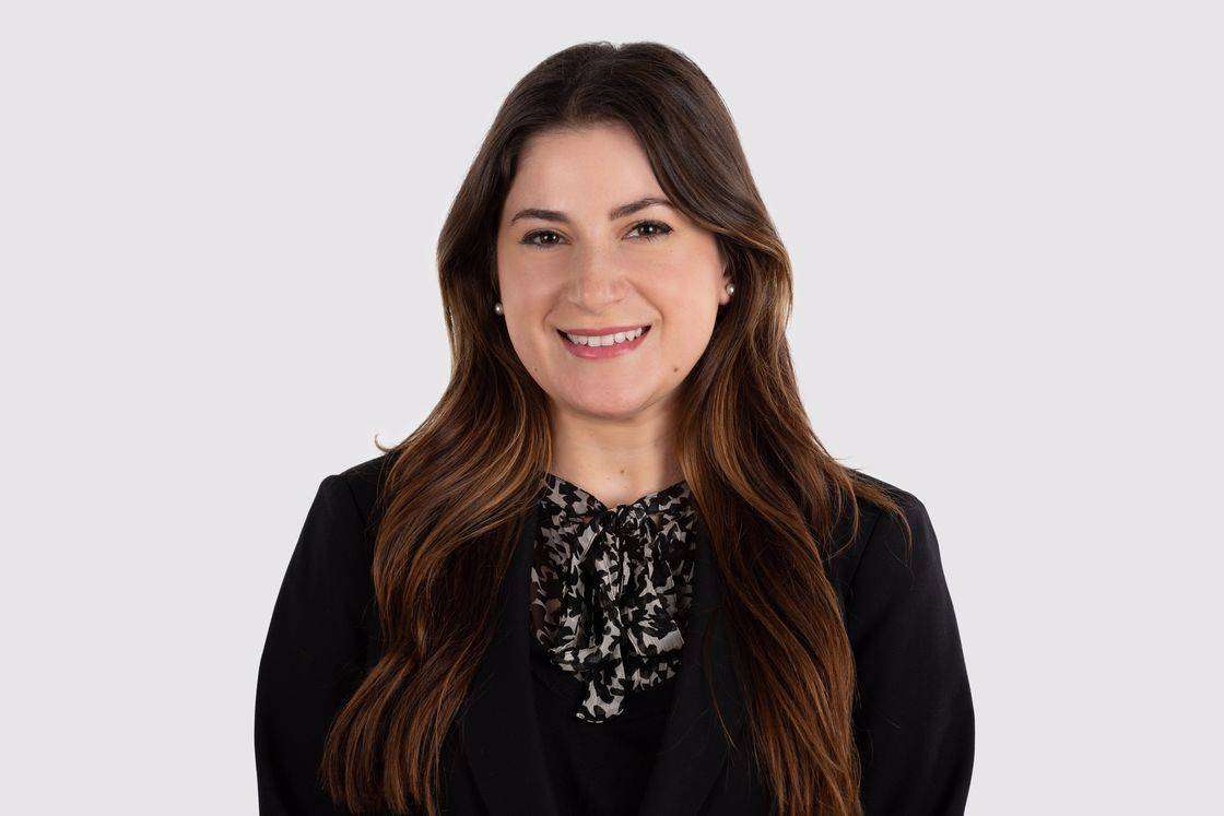 Woman wearing a black suit jacket and a printed black and white shirt posing for a headshot